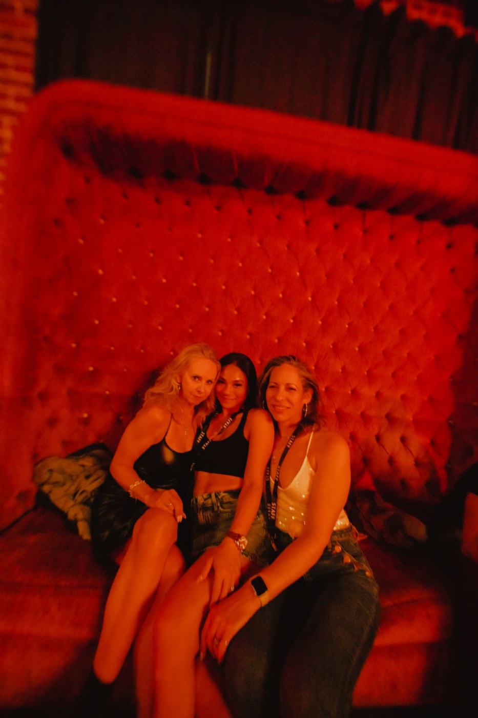 Three staff in lanyards sitting on a red velvet booth under red light