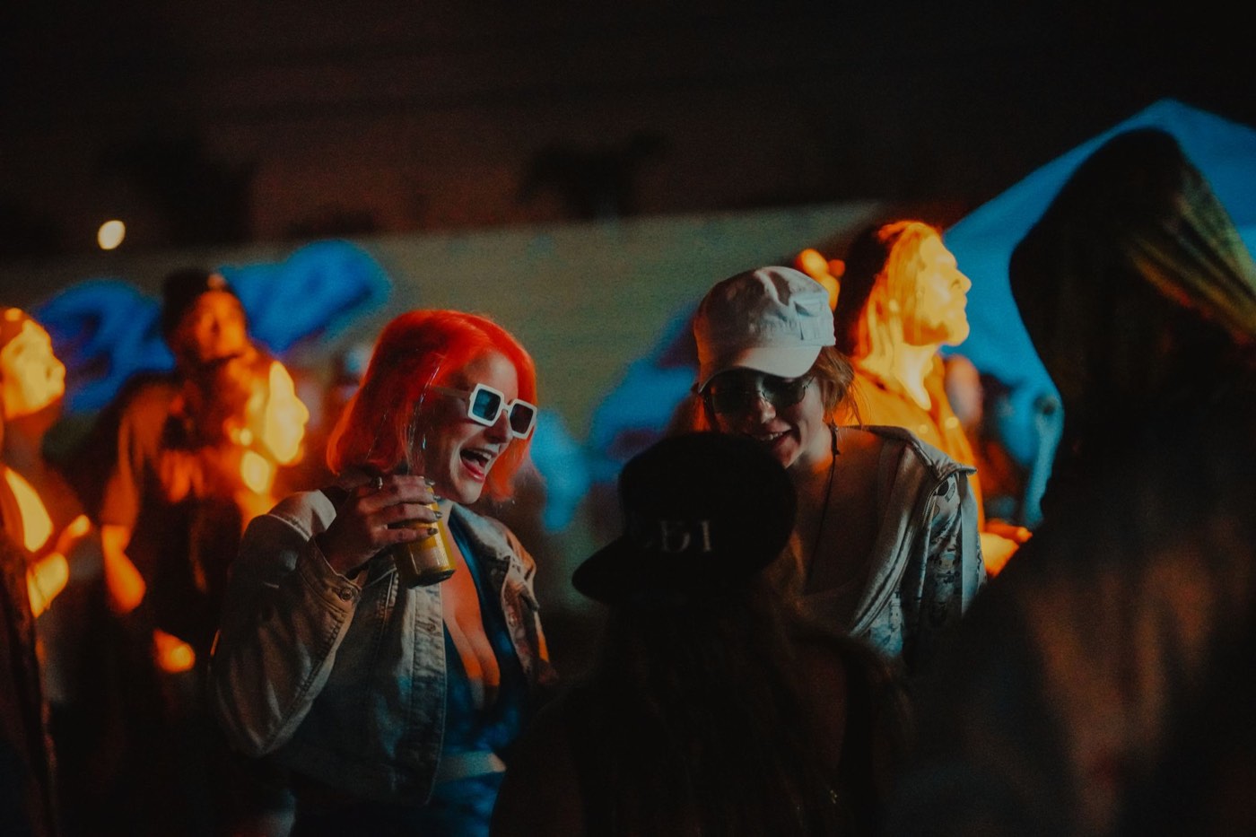 People laughing with drinks at night under orange and blue stage light