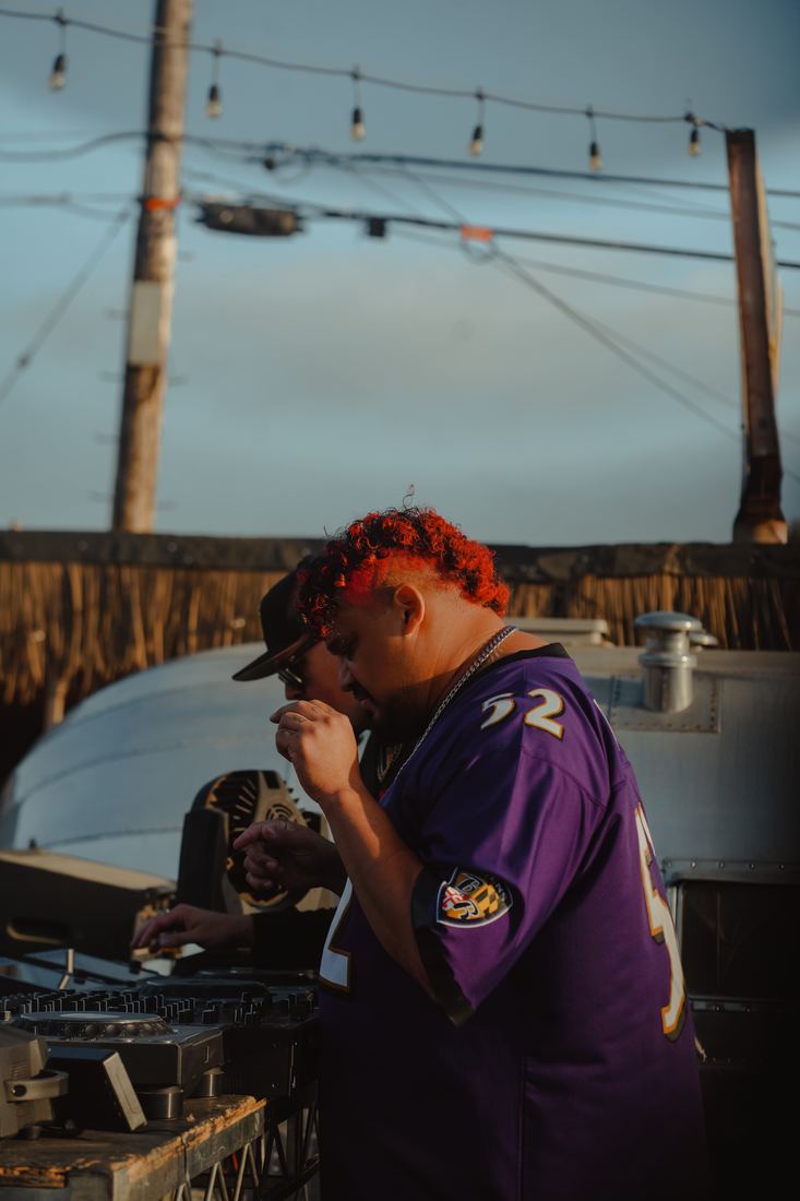 DJ in a purple jersey leaning over the decks