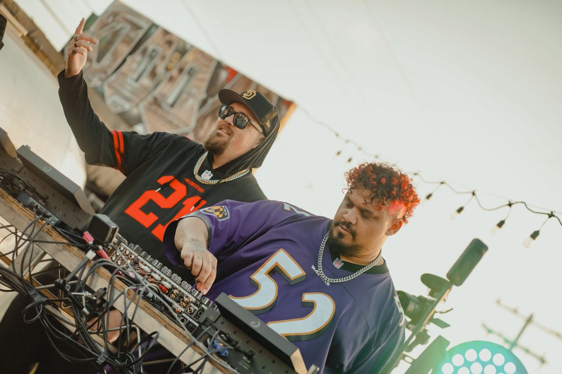 Two DJs at the decks seen from below, one in a number 52 jersey