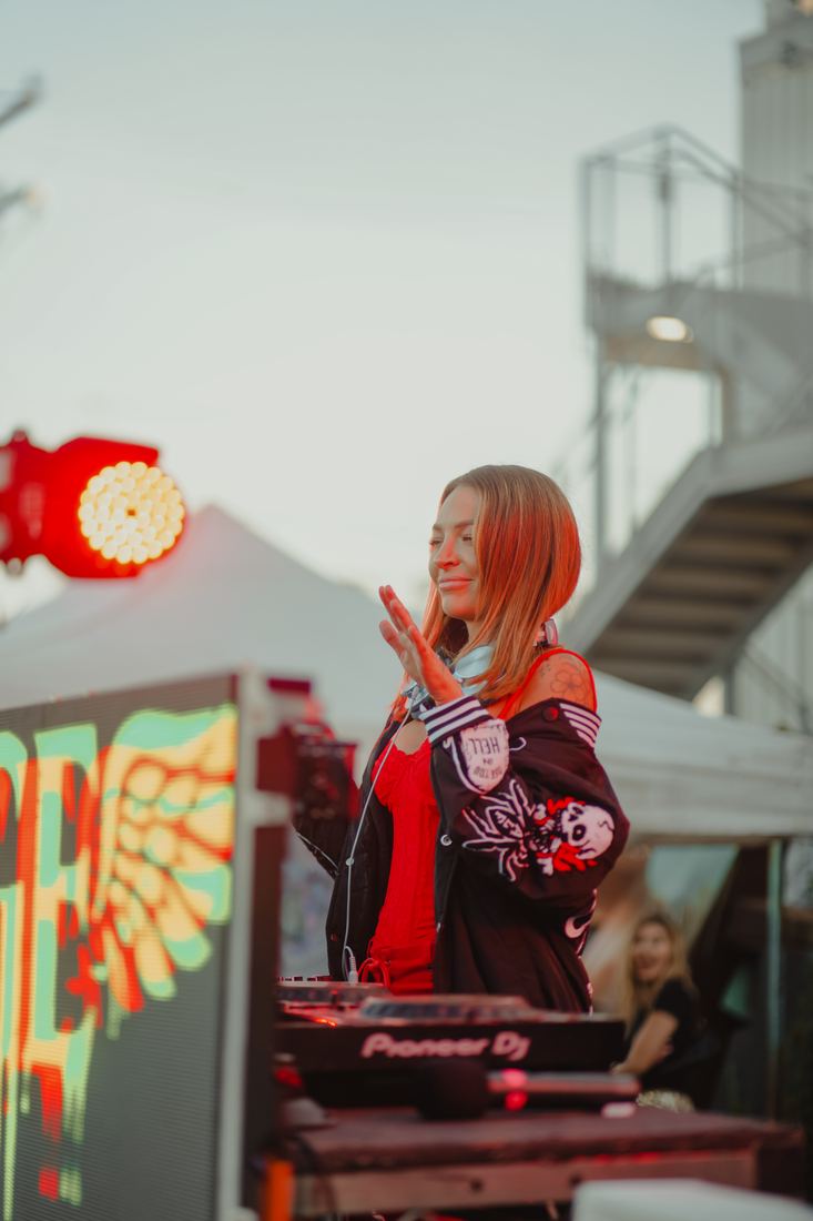 DJ with red hair playing beside a neon sign