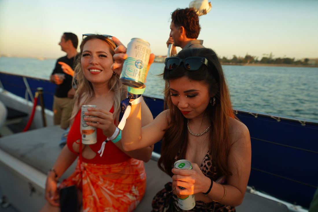 Two women on deck holding drinks with the water behind them
